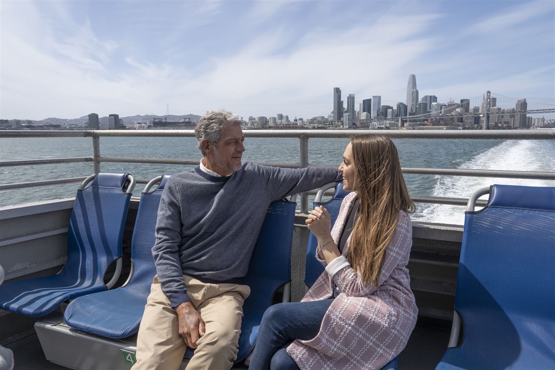 A man and a woman sitting on the outer seats of the ferry having a conversation