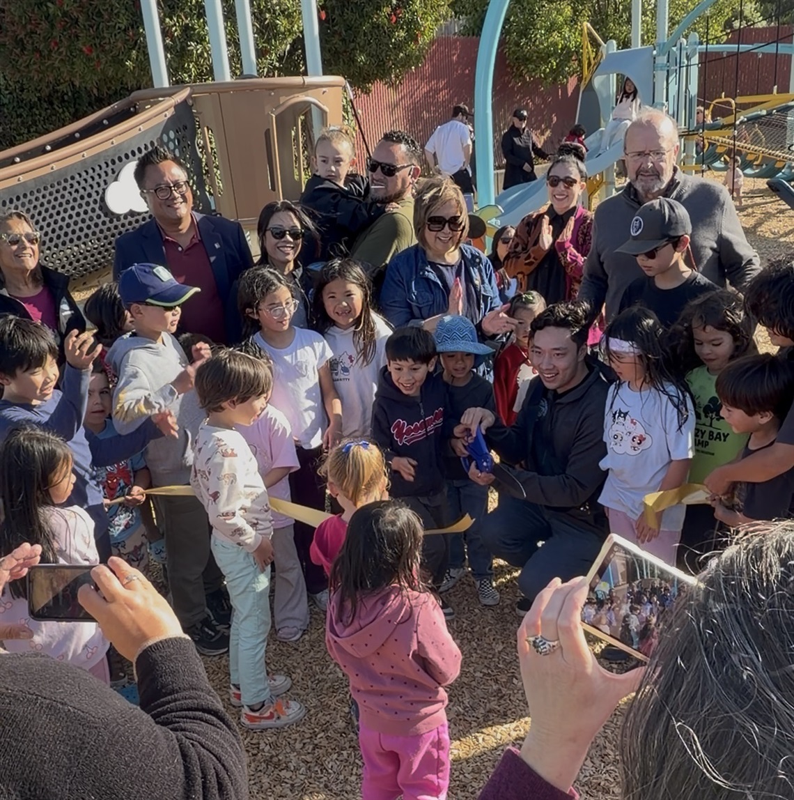 Children and community members surrounding Council while cutting the ribbon in front of the new Dundee Park play structure