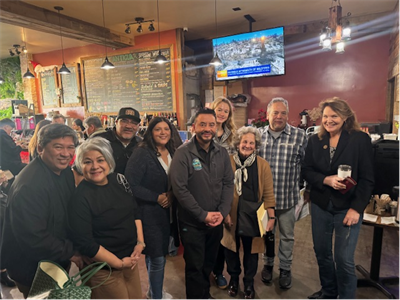 Mayor Eddie and City staff with residents at Antigua Cafe with a TV and menu behind them