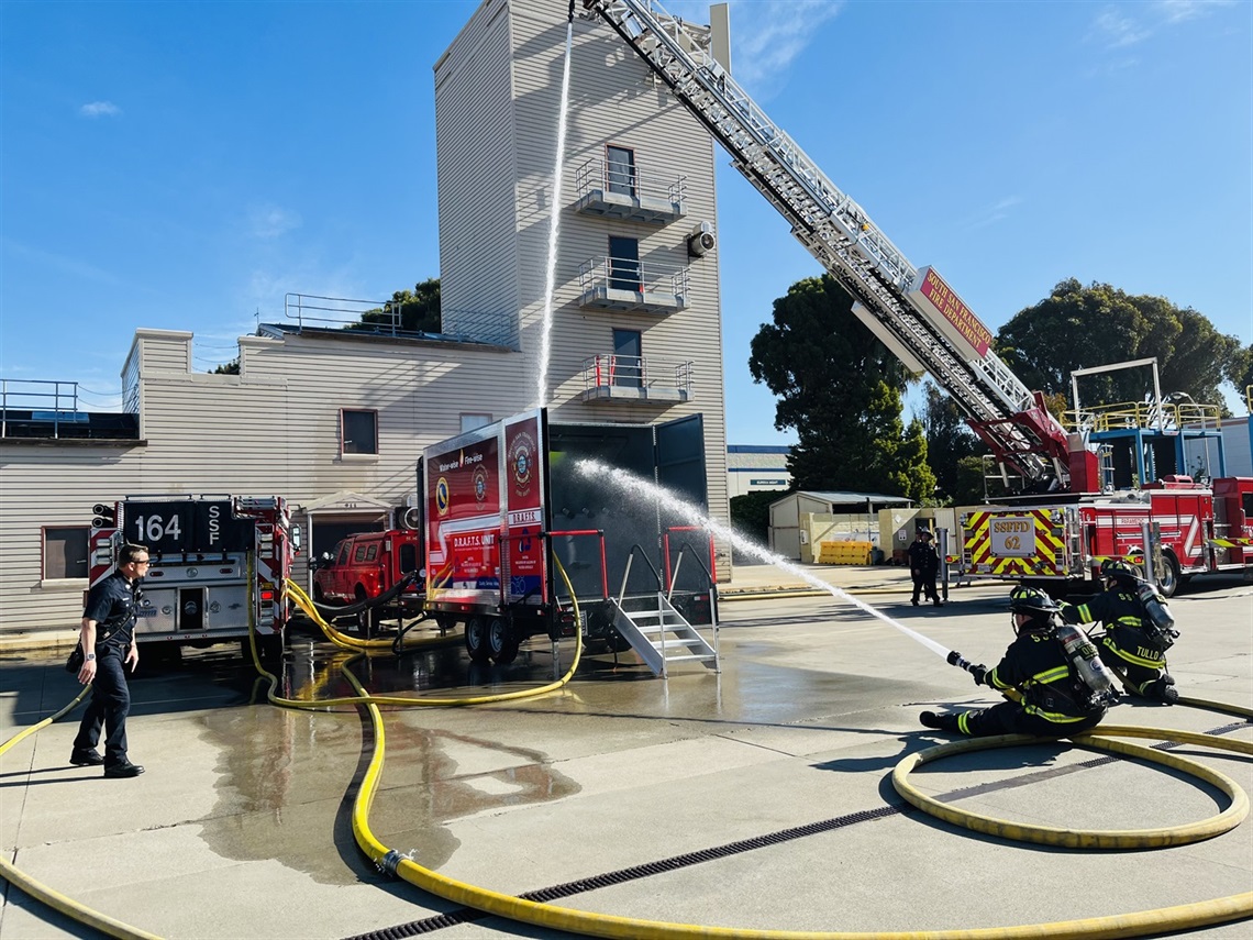 Two firefighters spraying water into the new DRAFTS unit via hose while the Fire Truck is spraying water down from the ladder