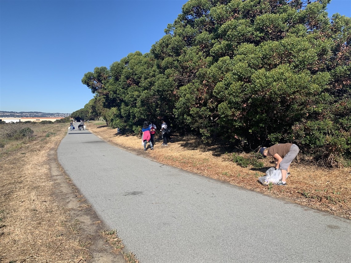 Volunteers picking up trash along Oyster Point Marina trail on Coastal Cleanup Day