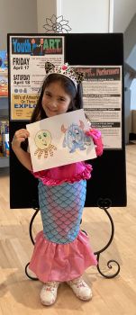 child in mermaid costume holds her art