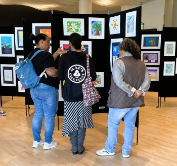Three ladies viewing a collection of flat art on panels