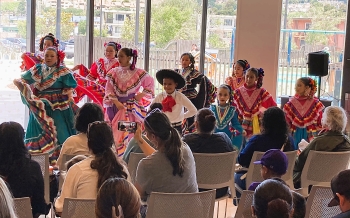 Ten children in Mexican folk costume dance in front of seated audience