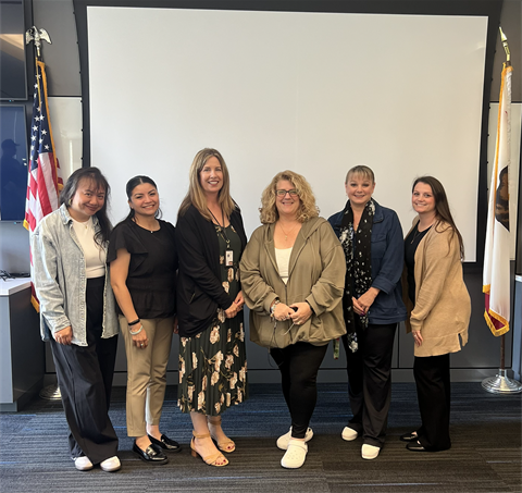 Six women who serve on the Dispatch Team taking a group photo in front of a projector screen