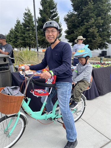 A dad riding his bike with his son riding behind him